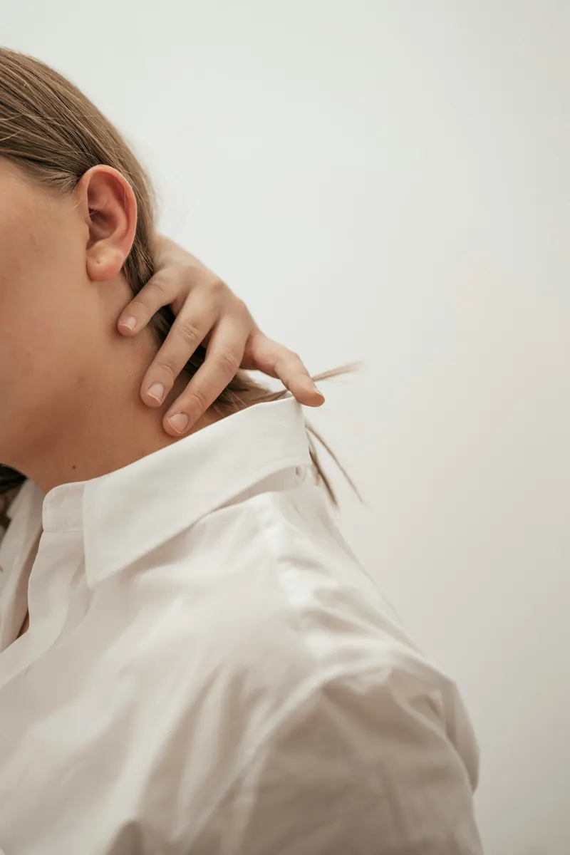 Person in a white shirt pressing a hand to the side of the neck, showing neck and jaw tension