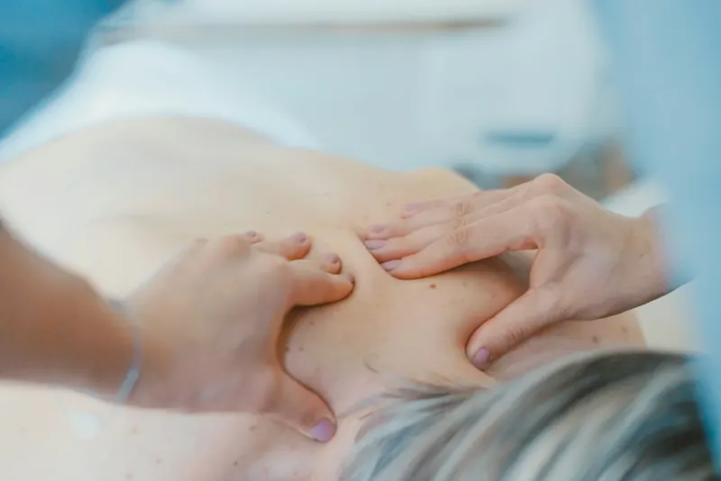 Hands working on the upper back and shoulder blade area during a manual therapy session