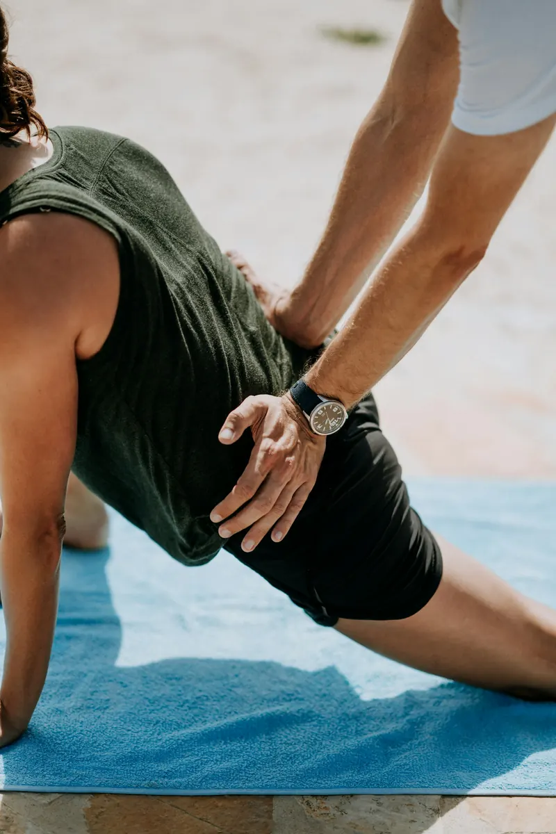 Practitioner assisting a kneeling client with a hip mobility exercise