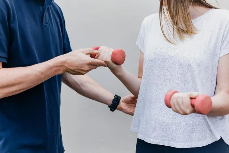 Practitioner guiding a client through a shoulder strengthening exercise with light dumbbells